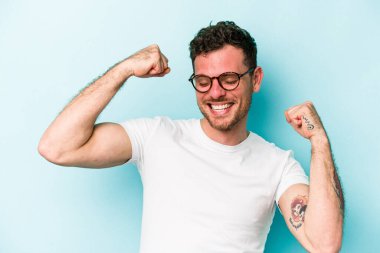 Kafkasyalı genç adam mavi arka planda izole edilmiş kaygısız ve heyecanlı tezahüratlar yapıyor. Zafer konsepti.