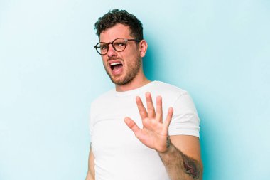 Mavi arka planda izole genç beyaz adam yakın bir tehlike nedeniyle şoka uğruyor