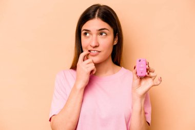 Latin kökenli genç bir kadın, elinde bej arka planda izole edilmiş bir araba tutuyor. Bir şeyin fotokopi odasına baktığını düşünüyor..