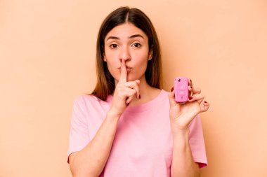 Latin kökenli genç bir kadın elinde bej arka planda izole edilmiş bir araba tutuyor ya sır saklıyor ya da sessizlik istiyor..