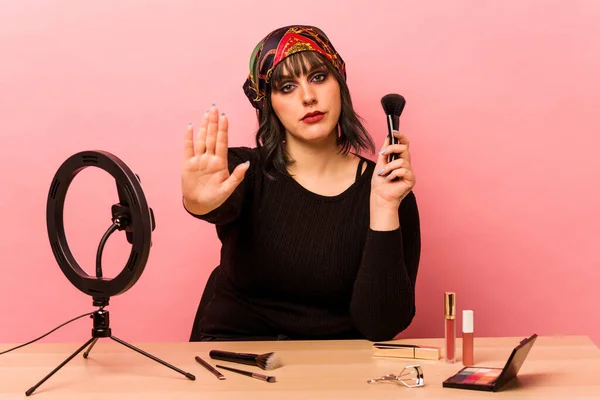 Young makeup artist woman doing a makeup tutorial isolated on pink background standing with outstretched hand showing stop sign, preventing you.