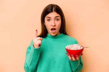 Latin kökenli genç bir kadın bej arka planda izole edilmiş mısır gevreği yiyor..