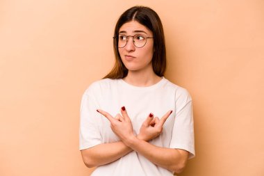 Latin kökenli genç bir kadın bej arka planda iki seçenek arasında seçim yapmaya çalışıyor..