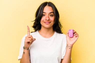 Pembe arka planda izole edilmiş anahtar taşıyan Latin kökenli genç bir kadın bir numarayı parmağıyla gösteriyor..