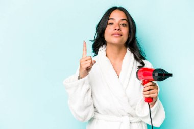 Elinde kurutucu tutan genç İspanyol kadın mavi arka planda bir numarayı parmağıyla gösteriyor..