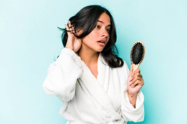 Mavi arka planda saç fırçası tutan genç İspanyol kadın bir dedikoduyu dinlemeye çalışıyor..