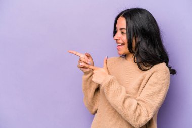 Genç İspanyol kadın mor arka planda izole edilmiş başparmak uzakta, gülüyor ve kaygısız.