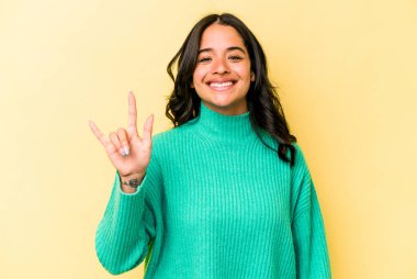 Sarı arka planda izole edilmiş genç İspanyol kadın boynuzlarını devrim konsepti olarak gösteriyor..