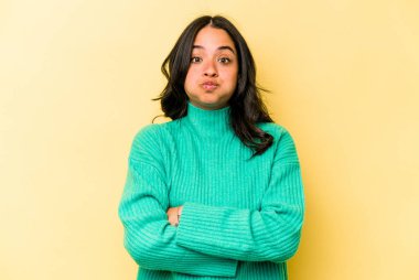 Sarı arka planda izole edilmiş genç İspanyol kadın yanakları patlatıyor, yorgun bir ifadesi var. Yüz ifadesi kavramı.