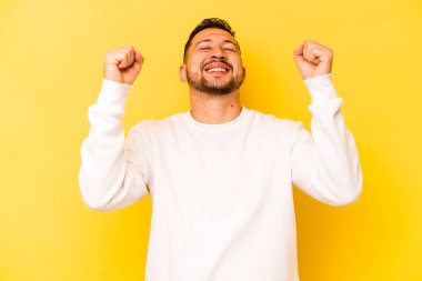Sarı arka planda izole edilmiş genç İspanyol bir adam zaferi, tutkuyu ve coşkuyu kutluyor, mutlu bir ifade..