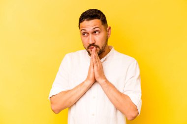 İspanyol asıllı genç adam sarı arka planda izole edilmiş dua ediyor, bağlılık gösteriyor, dindar biri ilahi ilhamı arıyor..
