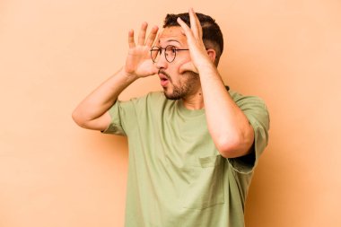 Latin kökenli genç bir adam, bej arka planda izole edilmiş. Başarı fırsatı bulmak için gözlerini açık tutuyor..