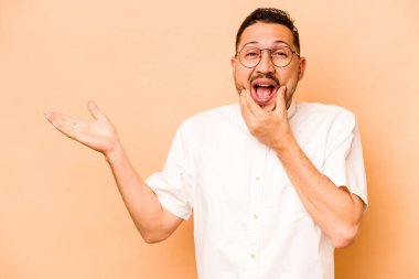 Bej arka planda izole edilmiş genç İspanyol bir adam avuç içinde fotokopi alanı tutuyor, el üstünde tutuyor. Şaşırmış ve mutlu..