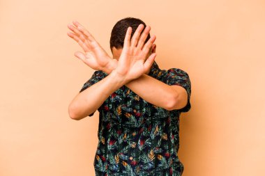 Latin kökenli genç adam bej arka planda izole edilmiş iki kolu çapraz tutuyor, inkar kavramı.