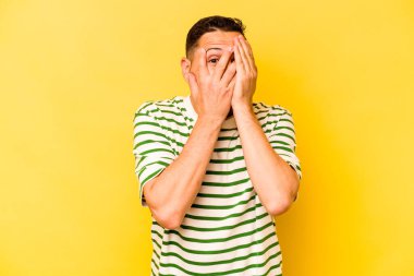 Sarı arka planda izole edilmiş genç bir İspanyol parmaklarıyla gözünü kırp korkmuş ve gergin..