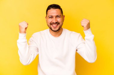 Genç İspanyol adam sarı arka planda izole edilmiş kaygısız ve heyecanlı tezahüratlar yapıyor. Zafer konsepti.