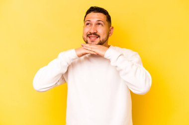 Sarı arka planda izole edilmiş genç İspanyol adam ellerini çenesinin altında tutuyor ve mutlu bir şekilde yan tarafa bakıyor..