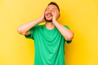 Sarı arka planda izole edilmiş genç İspanyol adam mutlu bir şekilde ellerini başının üstünde tutarak gülüyor. Mutluluk kavramı.