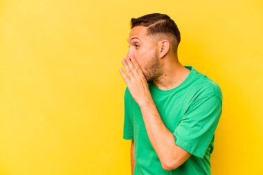 Genç İspanyol adam sarı arka planda izole edilmiş. Gördüğü bir şey yüzünden şoka uğruyor..