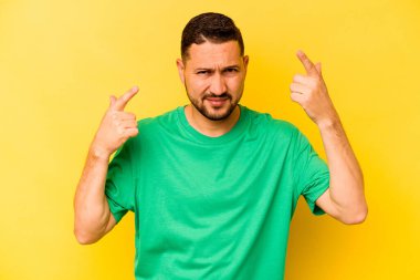 Sarı arka planda izole edilmiş genç İspanyol adam işaret parmağıyla bir hayal kırıklığı gösteriyor..