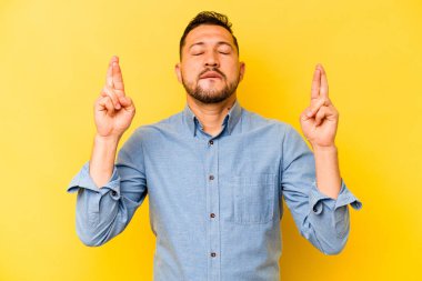 Genç İspanyol adam sarı arka planda izole edilmiş şans dilemek için şans diliyor.