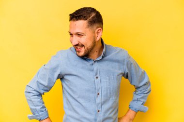 İspanyol asıllı genç adam sarı arka planda izole edilmiş. Kendine güveniyor. Kalçaları tutuyor..