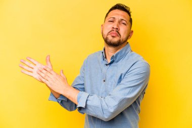 Genç İspanyol adam sarı arka planda izole edilmiş enerjik ve rahat hissediyor, ellerini ovuşturuyor kendinden emin..