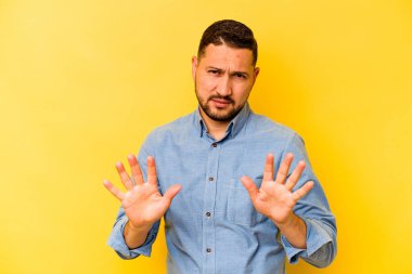 Latin kökenli genç bir adam, sarı arka planda izole edilmiş, tiksinti gösteren birini reddediyor..