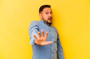 İspanyol genç adam sarı arka planda izole edilmiş. Yakın bir tehlike nedeniyle şoka uğruyor.