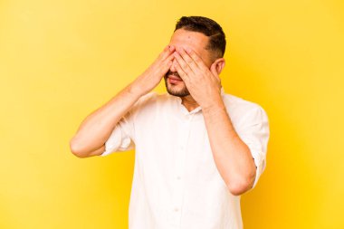 Sarı arka planda izole edilmiş genç İspanyol adam elleriyle gözlerini kapatmaktan korkuyor..