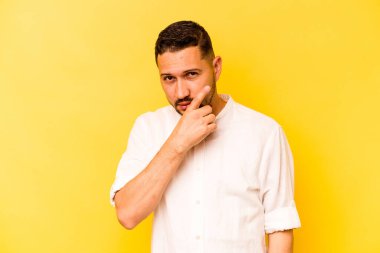 Latin kökenli genç bir adam sarı arka planda izole edilmiş. Bir strateji planlıyor, bir iş yolu düşünüyor..