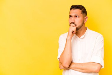 Genç İspanyol adam sarı arka planda izole edilmiş şüpheli ve şüpheci bir ifadeyle yana bakıyor..