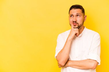 Genç İspanyol adam sarı arka planda izole edilmiş şüpheli ve şüpheci bir ifadeyle yana bakıyor..