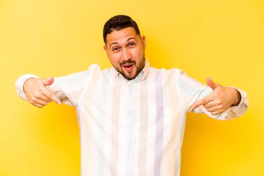 Latin kökenli genç adam sarı arka planda izole edilmiş. Parmakları aşağıda, olumlu hisler içinde..