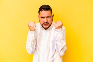 Sarı arka planda izole edilmiş genç İspanyol adam kameraya yumruk gösteriyor, agresif yüz ifadesi..