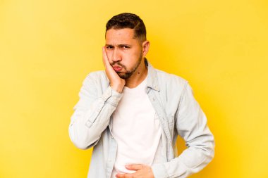 Sarı arka planda izole edilmiş genç İspanyol adam yanakları patlatıyor, yorgun bir ifadesi var. Yüz ifadesi kavramı.