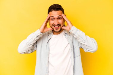 Latin kökenli genç adam sarı arka planda izole edilmiş. Hoş bir sürpriz bekliyor. Heyecanlı ve el kaldırıyor..