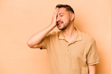 Latin kökenli genç adam bej arka planda izole edilmiş gülerek, kaygısız, doğal duygularla gülüyor..