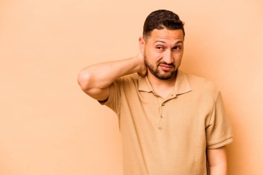 Latin kökenli genç adam bej arka planda izole edilmiş kafasının arkasına dokunuyor, düşünüyor ve bir seçim yapıyor..