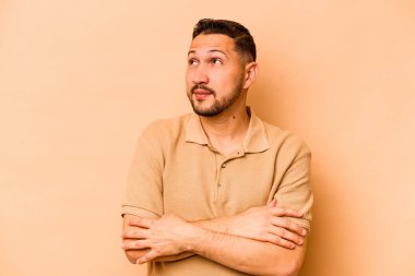 Latin kökenli genç adam bej arka planda izole edilmiş hedeflerine ve amaçlarına ulaşma hayali kuruyor.