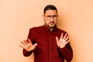 Latin kökenli genç bir adam, bej arka planda izole edilmiş, tiksinti belirtisi gösteren birini reddediyor..