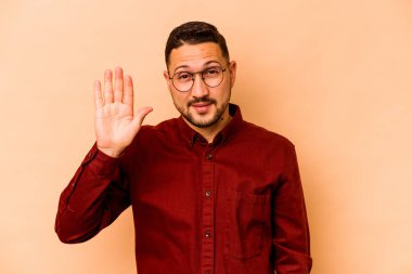 Latin kökenli genç adam bej arka planda izole edilmiş gülümsüyor beş numarayı parmaklarıyla gösteriyor..