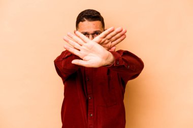 Latin kökenli genç bir adam, bej arka planda izole edilmiş, inkar hareketi yapıyor.