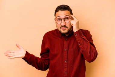 Latin kökenli genç bir adam bej arka planda izole edilmiş ve elinde bir ürün tutuyor..