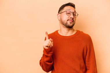 Latin kökenli genç bir adam bej arka planda izole edilmiş. Parmağıyla bir numarayı gösteriyor..