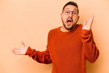 Bej arka planda izole edilmiş genç İspanyol bir adam avuç içinde fotokopi alanı tutuyor, el üstünde tutuyor. Şaşırmış ve mutlu..