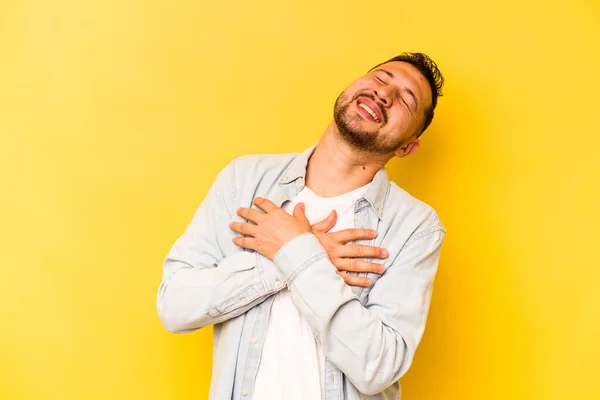 Młody Hiszpan Odizolowany Żółtym Tle Śmiał Się Trzymając Ręce Sercu — Zdjęcie stockowe