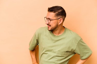 Latin kökenli genç adam bej arka planda izole edilmiş mutlu bir şekilde gülüyor ve elleri karnında gezdirirken eğleniyor..