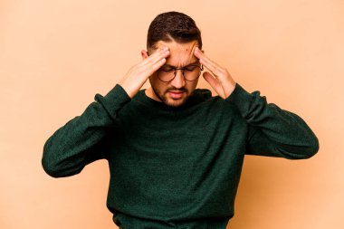 Latin kökenli genç adam bej arka planda izole edilmiş tapınaklara dokunuyor ve baş ağrısı çekiyor..