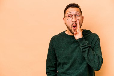 Latin kökenli genç adam, bej arka planda izole edilmiş bir şekilde gizli bir fren haberi veriyor.